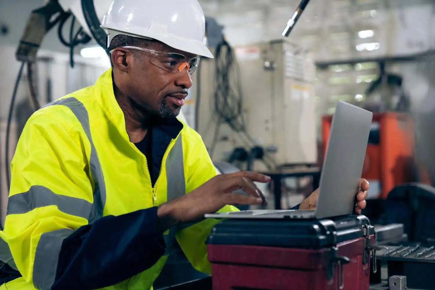 Homem em ambiente industrial planificando ou aprendendo como fazer plano de corte usando um laptop com foco e profissionalismo.