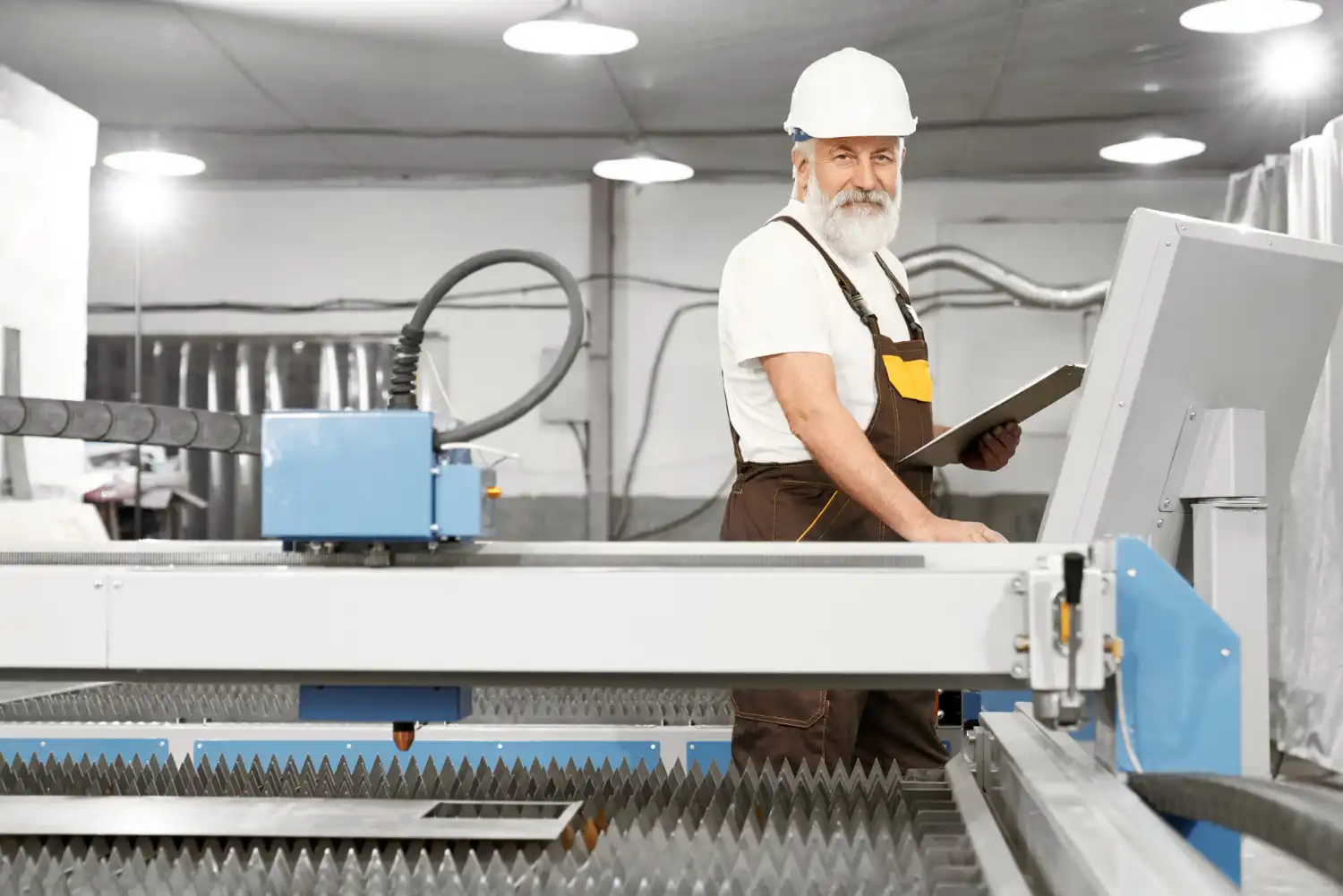 Homem idoso com uniforme de segurança trabalhando na indústria manufatureira, operando máquina de corte a laser em ambiente industrial moderno